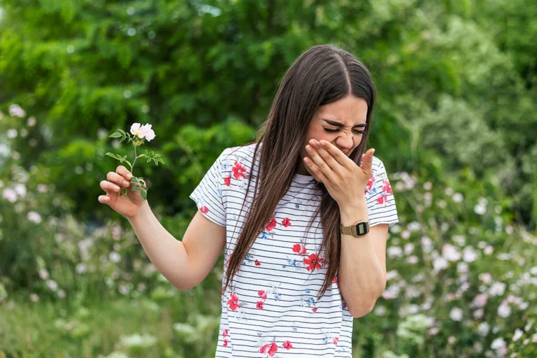 allergy future clinical studies - Young woman with Pollen allergy holding a flower and saying no.. Young woman with pollen and grass allergies. Flowering trees in background. Spring Seasonal allergies and health problems.